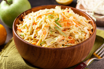 Cabbage salad. Homemade salad of cabbage, carrots and apples in a wooden bowl on a dark background. Vegan or diet food.