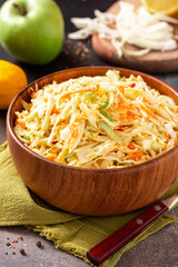 Cabbage salad. Homemade salad of cabbage, carrots and apples in a wooden bowl on a dark background. Vegan or diet food.