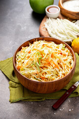 Cabbage salad. Homemade salad of cabbage, carrots and apples in a wooden bowl on a dark background. Vegan or diet food.