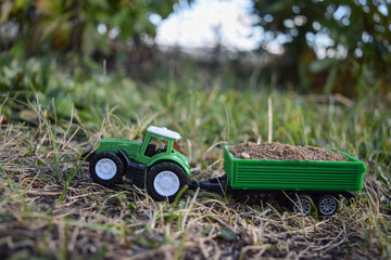 Fototapeta premium In the green grass there is a small green toy tractor with a trailer loaded with sand