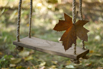 Big yellow-brown maple leaf on a swing on a background of blurred grass covered with autumn foliage