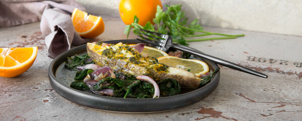 a plate of baked halibut steak with orange sauce and spinach on the table