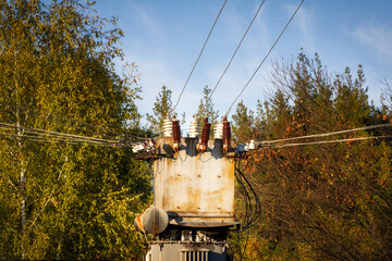 Electricity transformer booth in the forest. Autumn landscape with blue sky. Insulators and wires.