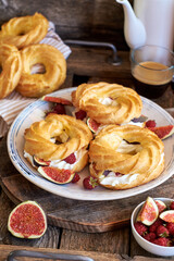 Obraz na płótnie Canvas Choux rings with cream, figs and raspberries. Wooden background, side view.