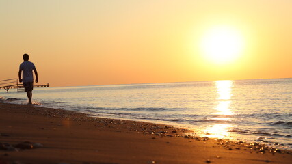 Fototapeta na wymiar Young man walking on the beach at sunset
