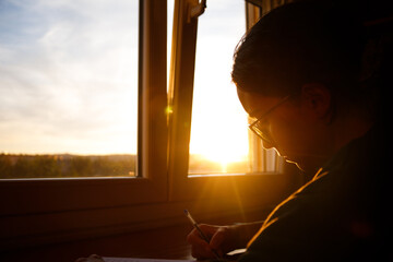 side view of silhouette of girl with glasses studying in her room during sunset