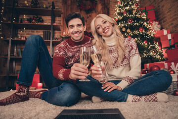 Full length photo of funny couple look screen cheers sit on carpet wear pullovers jeans socks indoors on x-mas eve