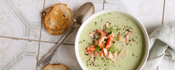 a bowl of broccoli cream soup with crayfish tails on a light table