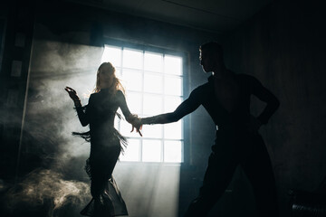 Couple of two professional ballroom dancers is dancing on loft studio. Beautiful art performance with heavy smoke. Sport life concept. Passion and emotional dance.