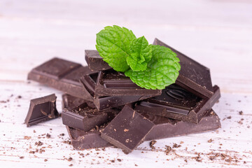 Pieces of bitter dark chocolate with green mint on a white wooden background. Close-up.