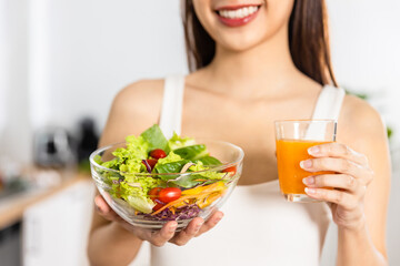 Close up Happy Asian healthy woman smiled and holding glass of orange juice and vegetable salad to diet and eat clean food