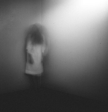 Ghost girl in white nightgown standing in corner of room at home