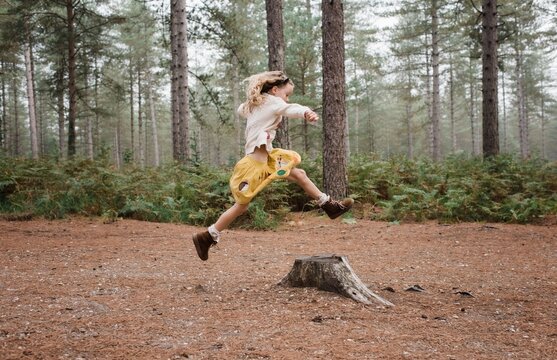 girl jumping over a tree stump in the forest in autumn