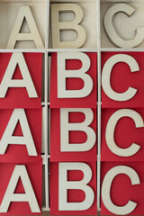 ABC repeated multiple times in a shallow wooden box with red paper squares