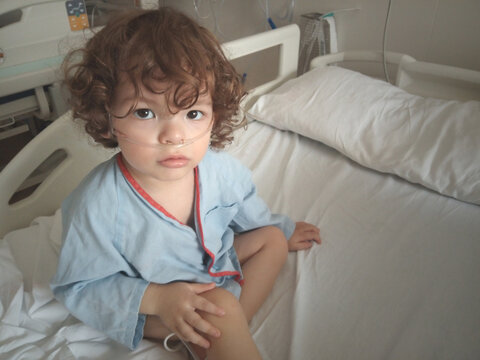 Niño de 2 años sentado en una cama de hospital, enfermo de bronquiolitis causada por bocavirus, con aporte de oxígeno mediante gafas nasales o cánula nasal.
