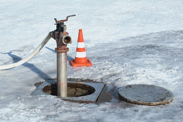 An open manhole, a pump and a traffic cone in winter.