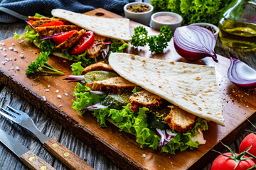 Italian piada wraps - piadina stuffed with fresh vegetables and roast chicken breast  on wooden table
