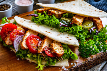 Italian piada wraps - piadina stuffed with fresh vegetables and roast chicken breast  on wooden table
