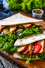Italian piada wraps - piadina stuffed with fresh vegetables and roast chicken breast  on wooden table
