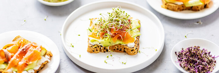 Flat lay top view of healthy sandwich with smoked salmon, cucumber, cream cheese and fresh microgreens alfalfa sprouts on white plate on gray concrete background. Healthy lifestyle. Growing sprouts