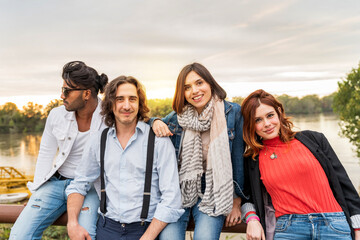 group of best friend have fun in front of a big river in autumn at sunset - obrazy, fototapety, plakaty