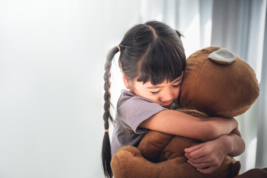 Blurred soft images of Asian girl is 6-year-old, is hugging a big brown teddy bear, in loneliness and sad, On white background, to children and family concept.