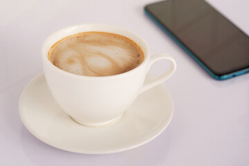 Fototapeta na wymiar White latte coffee mug, side view on white desk and mobile phone