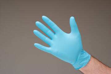 Disposable blue latex glove worn by Caucasian male hand. Close up studio shot, isolated against gray background