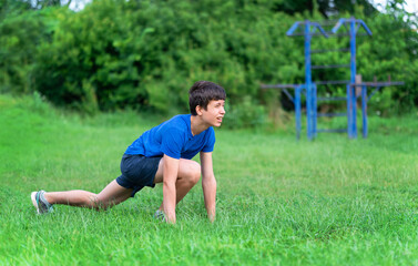 teenage boy exercising outdoors, sports ground in the yard, he squats and does a warm-up, healthy...