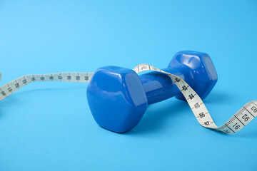 Fitness concept. Blue dumbbell weighing 1 kg and measuring tape on blue background