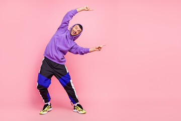 Full length photo of cool young brunet guy point empty space wear hoodie pants shoes isolated on pink background