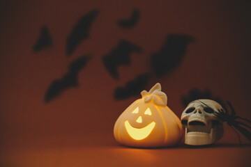 Halloween background. Glowing Jack o lantern pumpkin decoration and skull with spider on orange...