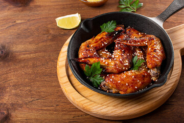  Baked chicken wings with sesame seeds, parsley and lime on a black pan and wooden background