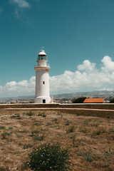 Lighthouse on the coast. Town in the background. White tower, blue sky, summer day. 