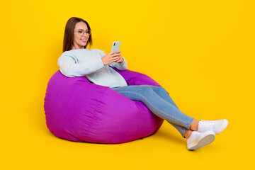Full size photo of happy woman enjoy sit chair hold phone good mood isolated on yellow color...