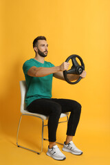 Serious man on chair with steering wheel against yellow background