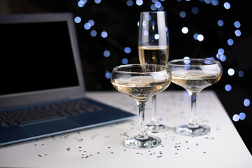 Glasses with champagne and laptop on light bokeh background, work on the holiday, celebration in office.