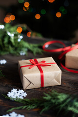 Christmas gift in craft paper, present on wooden table and light bokeh background, holiday concept.