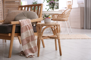 Stylish wooden stool with bouquet of flowers near armchair in room. Interior element