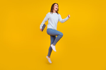 Full body photo of brunette haired stylish trendy lady hold laptop run empty space jump isolated on yellow color background