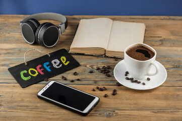 Fototapeta na wymiar A cup of coffee, headphone, open book and a board with the inscription 