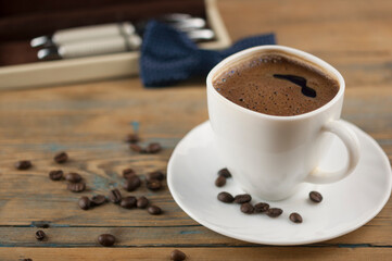A cup of coffee with bow tie and gift box on old wooden table with some beans. Father day card.