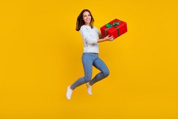 Fototapeta na wymiar Full body photo of happy cheerful young woman jump up hold hands holiday gift isolated on yellow color background