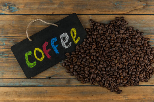 Heap coffee beans and a board with the inscription "coffee" written in a colorful alphabet. Coffee break, the concept of waking up in the morning.