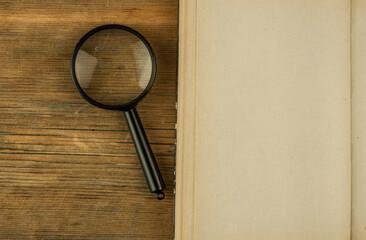 Magnifying lens with open book on wood desk.