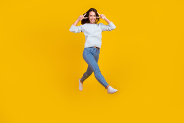 Full length photo of happy positive young woman jump up walk make v-signs cool isolated on yellow color background
