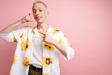 Young blonde man pointing finger aside and making handset gesture