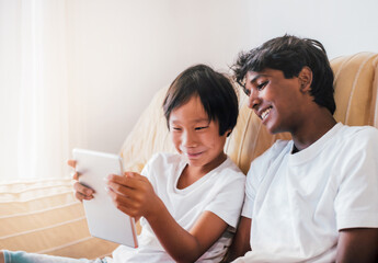 two boys of multiethnic origin have fun with a tablet in their living room. concept of diversity and technology in the family.