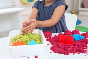 Little girl playing with bright kinetic sand at table indoors, closeup