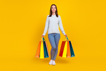 Full body photo of happy cool woman hold hands shopping bags smile isolated on yellow color...